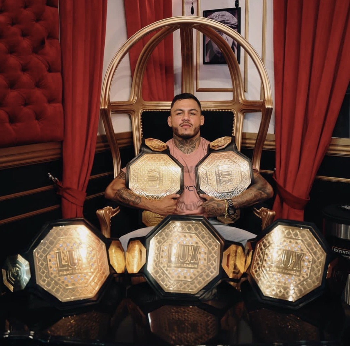 Marco Beltrán seated on a throne with multiple LUX title belts